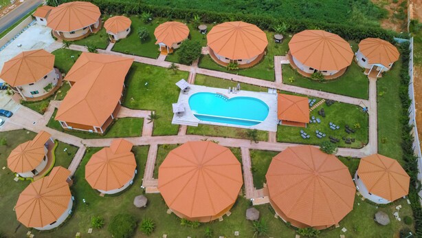 An aerial view of a resort with multiple round-roofed buildings, a central swimming pool, and a well-maintained lawn. - Eklôfè Bungalows Hôtel  (Yamoussoukro)