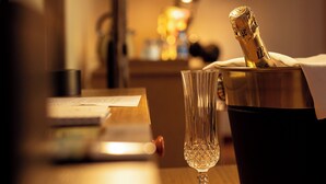 A wooden table with a bottle of champagne, a glass, and a lamp in a hotel room. - Eklôfè Bungalows Hôtel  (Yamoussoukro)