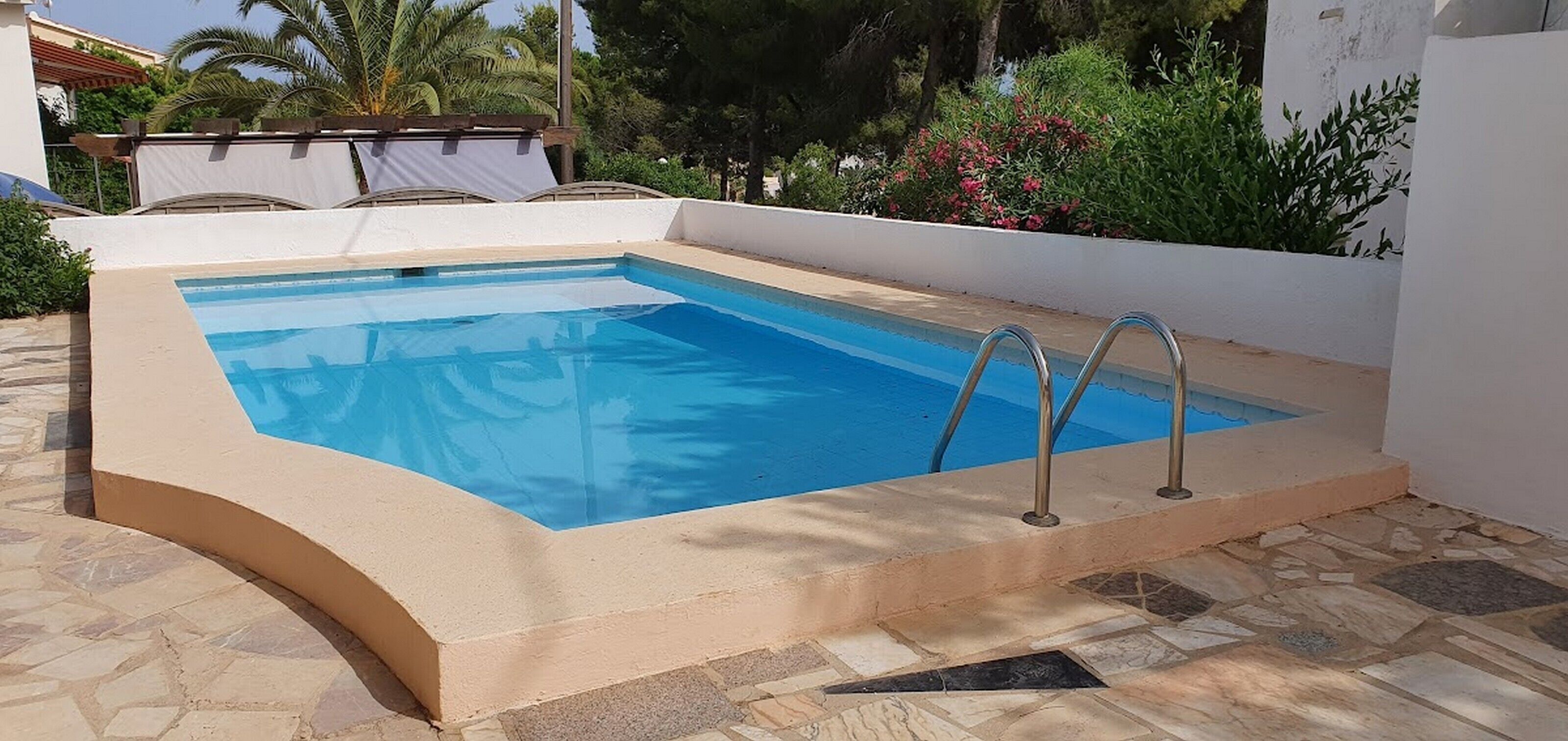 En rektangulær swimmingpool med en buet kant, omgivet af en beige mur og stenfliser.