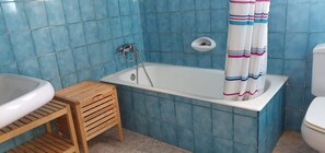 Une salle de bain avec une baignoire, un tabouret en bois et des toilettes.