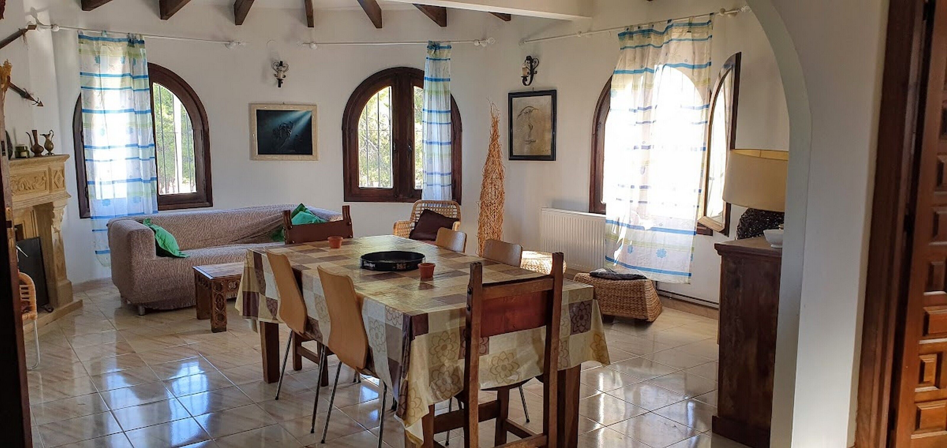 A dining area with a table and chairs, a sofa, and two windows with curtains.