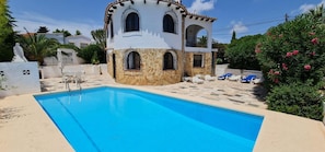 Un’area piscina con un edificio in pietra, una piscina azzurra cristallina e lettini da relax.