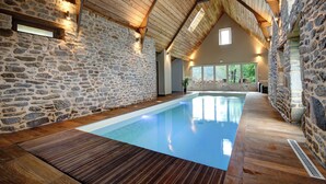 Une piscine intérieure aux murs en pierre et aux poutres en bois, entourée d’un plancher en bois.