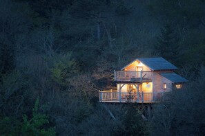 Een houten chalet met twee verdiepingen en een balkon, omringd door dicht bos.