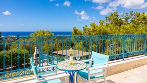 A balcony with a blue railing, a round table with chairs, and a bottle of wine. - Villa Ermis in Peyia (Pegeia)