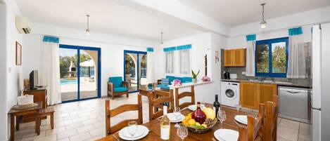 A spacious dining area with a wooden table set for six, a kitchen with modern appliances, and a view of the pool through the glass doors.