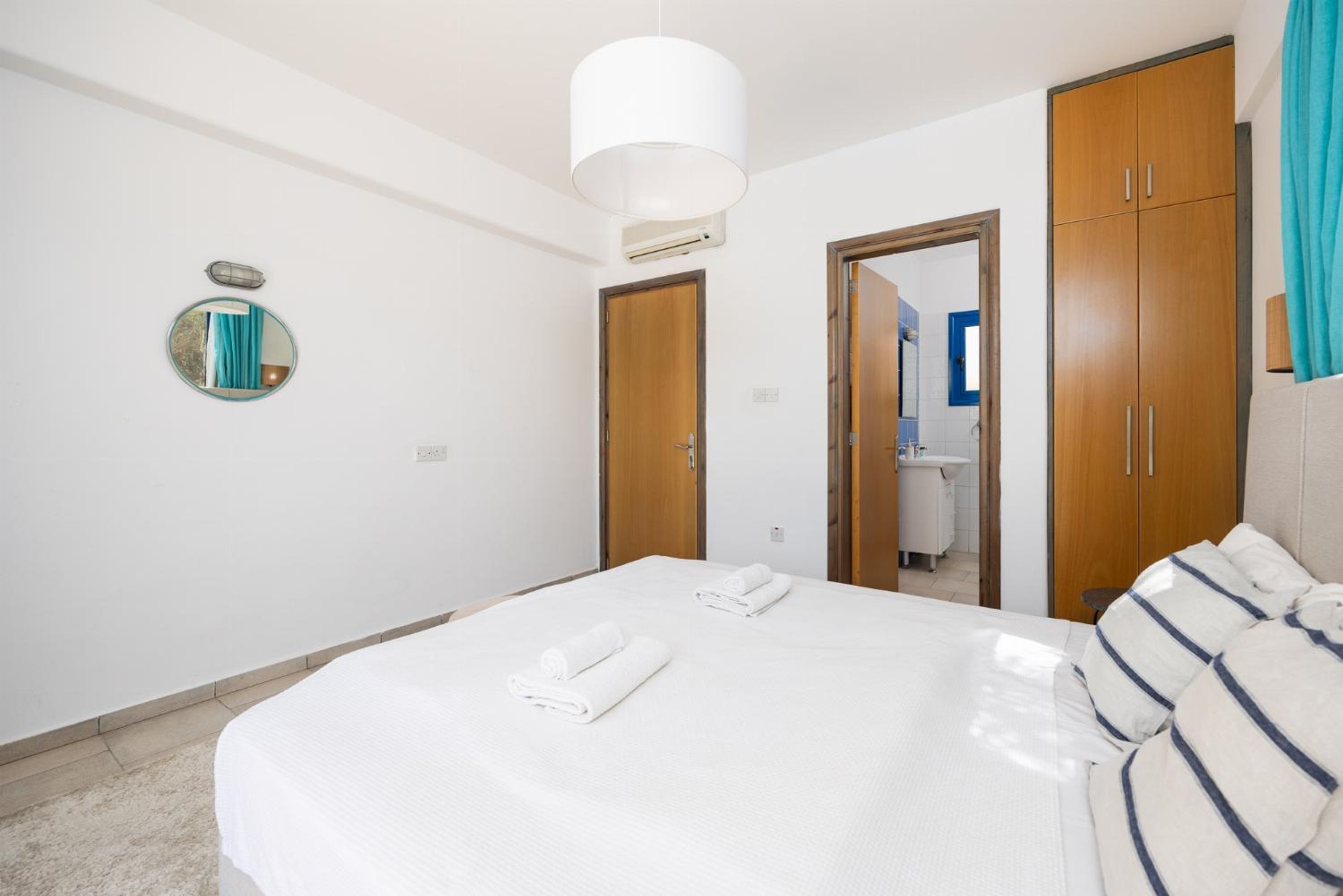 Une chambre d’hôtel avec un grand lit, un miroir rond, des armoires en bois et une porte donnant sur une salle de bain.
