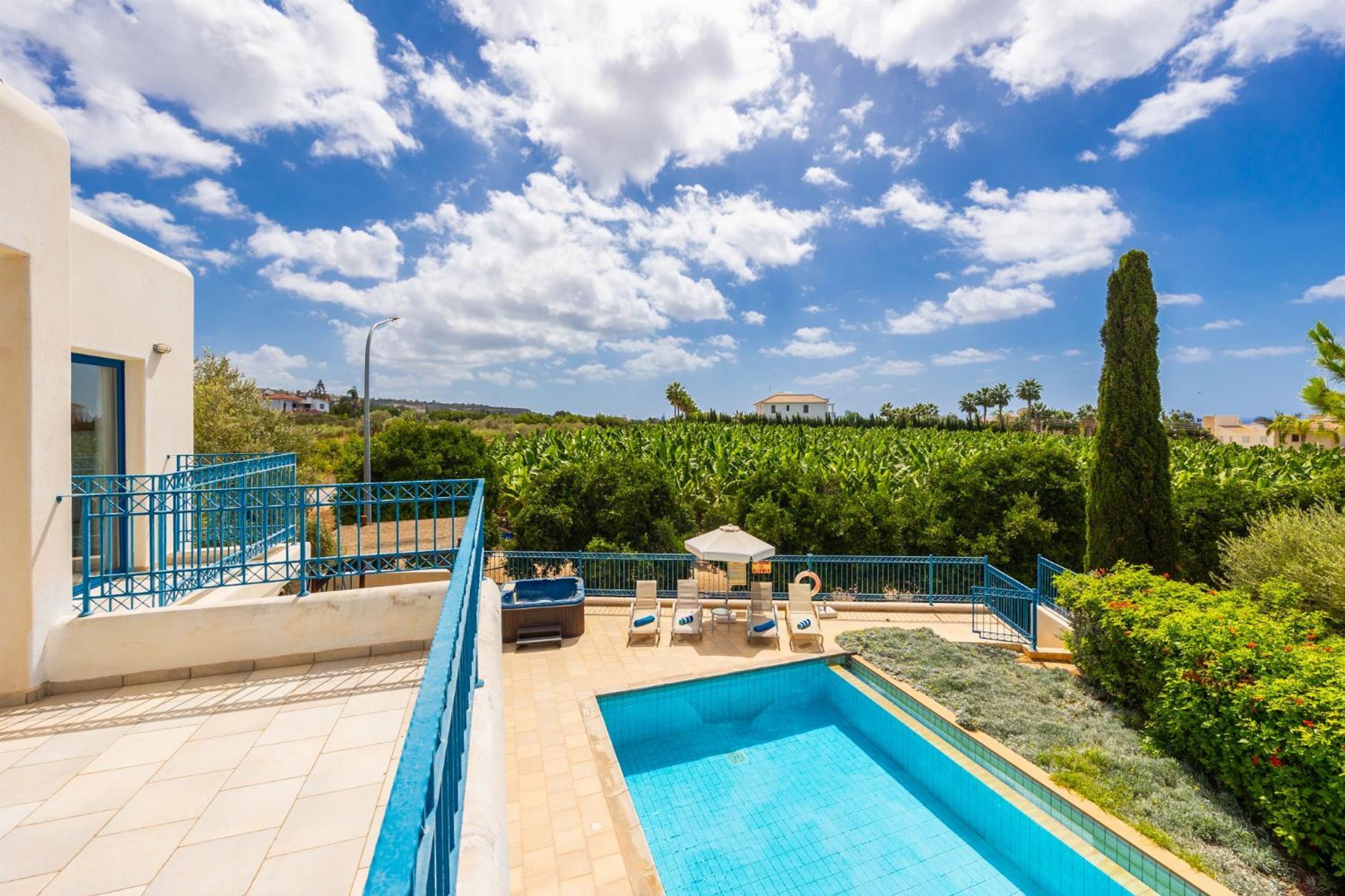 A swimming pool with lounge chairs and a sun umbrella, surrounded by greenery and a clear sky.