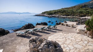 Une zone côtière dotée d’une terrasse en pierre, de chaises longues et d’un rivage rocheux.