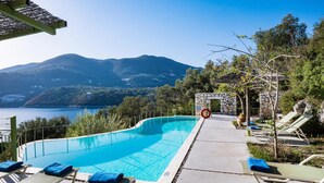 Une piscine dotée de chaises longues et d’un poste de surveillance pour les sauveteurs, entourée de montagnes et offrant une vue sur la mer.