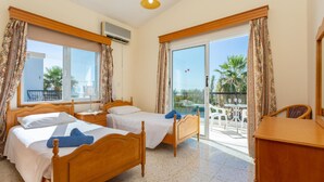 Ein Hotelzimmer mit zwei Holzbetten, einem Balkon mit Tisch und Stühlen sowie Blick auf Palmen.