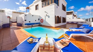 A pool area with blue lounge chairs, a lifebuoy, and a bottle of alcohol on a tray. - Villa Dulce in Tias With 4 Bedrooms and 2 Bathrooms (Tías)