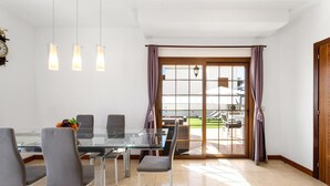A modern dining area with a glass table, grey chairs, and pendant lights. - Las Caletas in Teguise (Teguise)