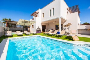 Una casa moderna de dos pisos con piscina, mobiliario exterior y una pérgola.