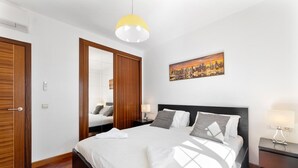 A modern hotel room with a large bed, wooden wardrobe, and a cityscape painting on the wall. - Las Caletas in Teguise (Teguise)
