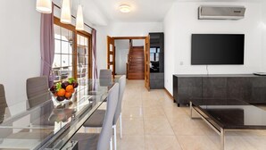 A modern living room with a glass dining table, a flat-screen TV mounted on the wall, and a staircase leading to another level. - Las Caletas in Teguise (Teguise)