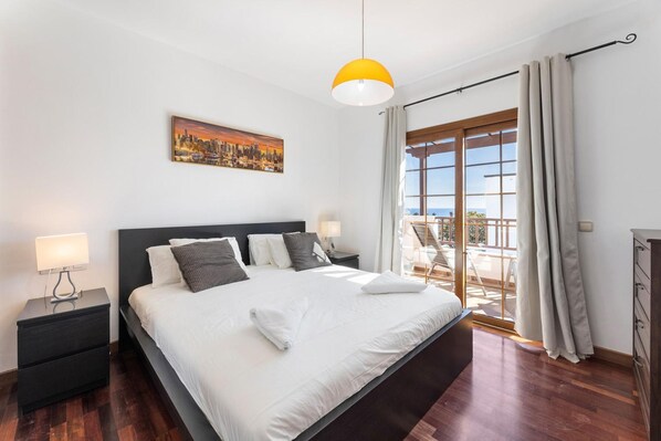 A modern bedroom with a large bed, a cityscape painting, a balcony with curtains, and a yellow pendant light. - Las Caletas in Teguise (Teguise)