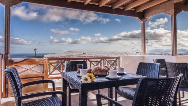 A terrace with wicker furniture, a table set with a croissant, coffee cups, and a flower. - Casa Morro Blanco in Conil (Tías)