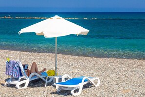 A beach with two white lounge chairs, one with a blue cushion, and a white umbrella providing shade. - Villa Christos in Argaka (Argaka)