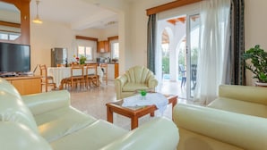 A spacious living area with a sofa, a coffee table, and a television. There is a dining area with a table and chairs, and a kitchen in the background. - Villa Christos in Argaka (Argaka)