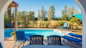 A pool area with blue lounge chairs and a pergola, surrounded by trees and a view of the sea. - Villa Christos in Argaka (Argaka)