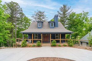 A two-story house with a gabled roof, a front porch with wooden railings, and a chimney.