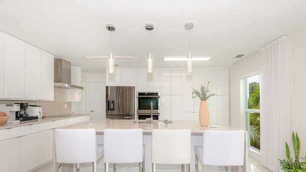 A modern kitchen with white cabinetry, stainless steel appliances, and a central island with bar stools. - Luxury Beach Home Salt Water Pool Kid Pet Friendly (Boca Raton)