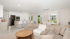 A modern living room with a sectional sofa, a wooden coffee table, and a kitchen area with stainless steel appliances. - Luxury Beach Home Salt Water Pool Kid Pet Friendly (Boca Raton)