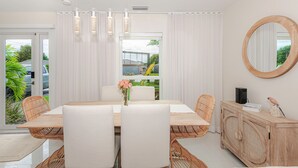 A modern dining area with a glass table, white chairs, and a wooden cabinet. - Luxury Beach Home Salt Water Pool Kid Pet Friendly (Boca Raton)