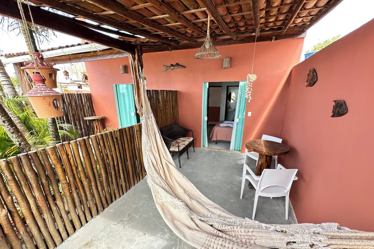 A hammock under a wooden roof, a small table with chairs, and a door leading to a room.