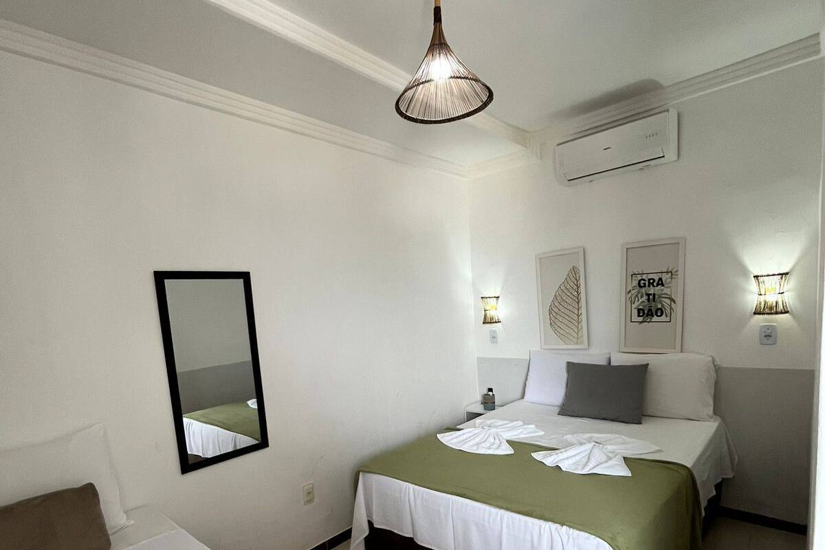 A hotel room with a bed, a bedside table, a mirror, and a wall-mounted air conditioner.