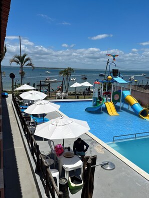 A pool area with a water slide and umbrellas, overlooking a body of water with boats. - Pousada Mar da Gamboa (Cairu)