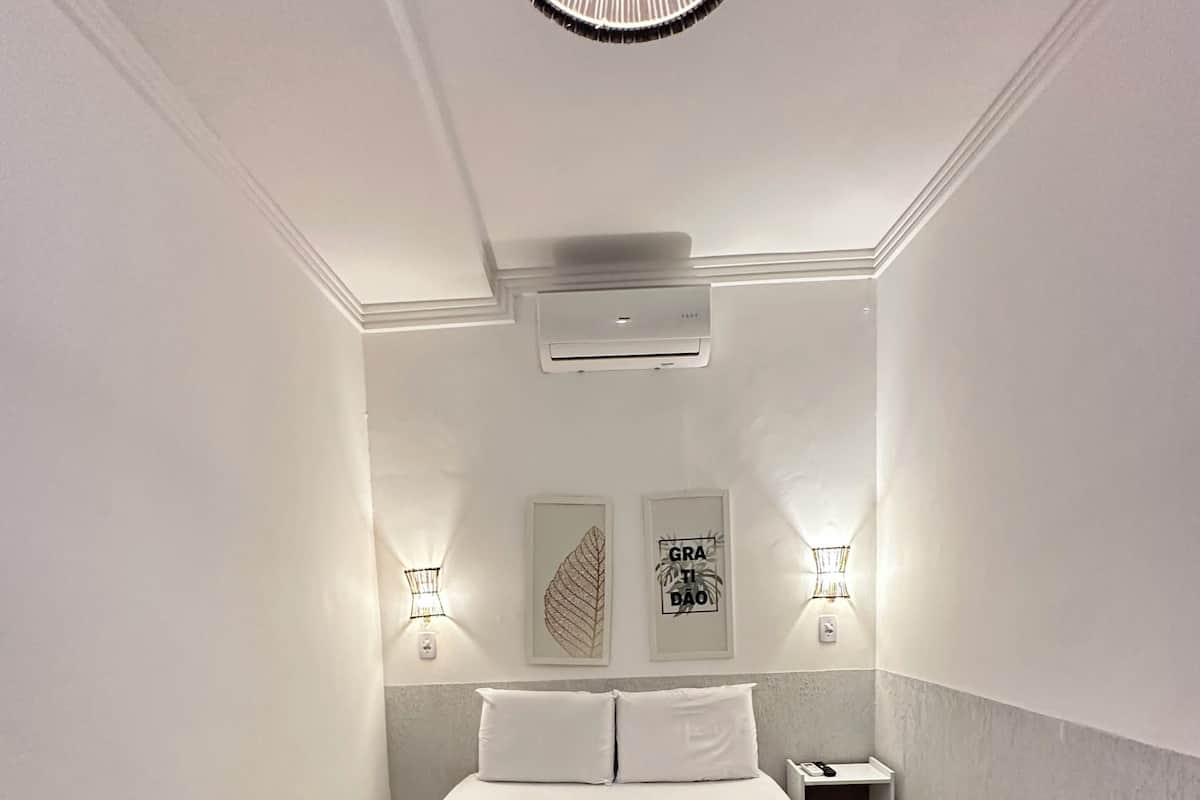 A modern hotel room with a bed, air conditioning unit, wall-mounted lights, and artwork.