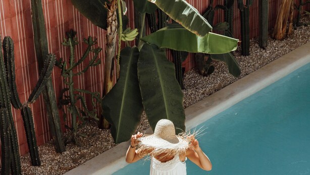 A person in a white dress walking into a pool area with a large plant and cacti in the background. - CASA OHMA, an elegant Maison de Charme with swimming pool in La Punta (Punta de Zicatela)