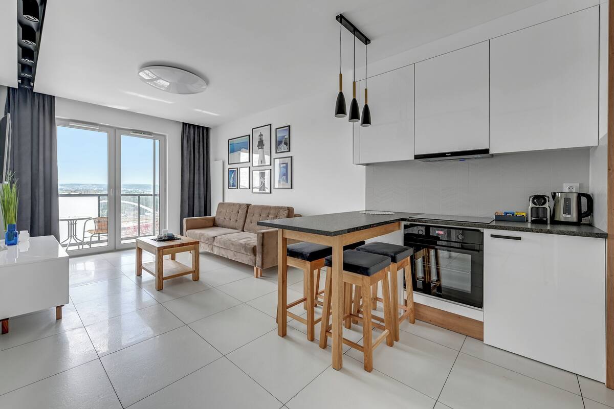 A modern kitchen with a central island, bar stools, and a dining area with a sofa.
