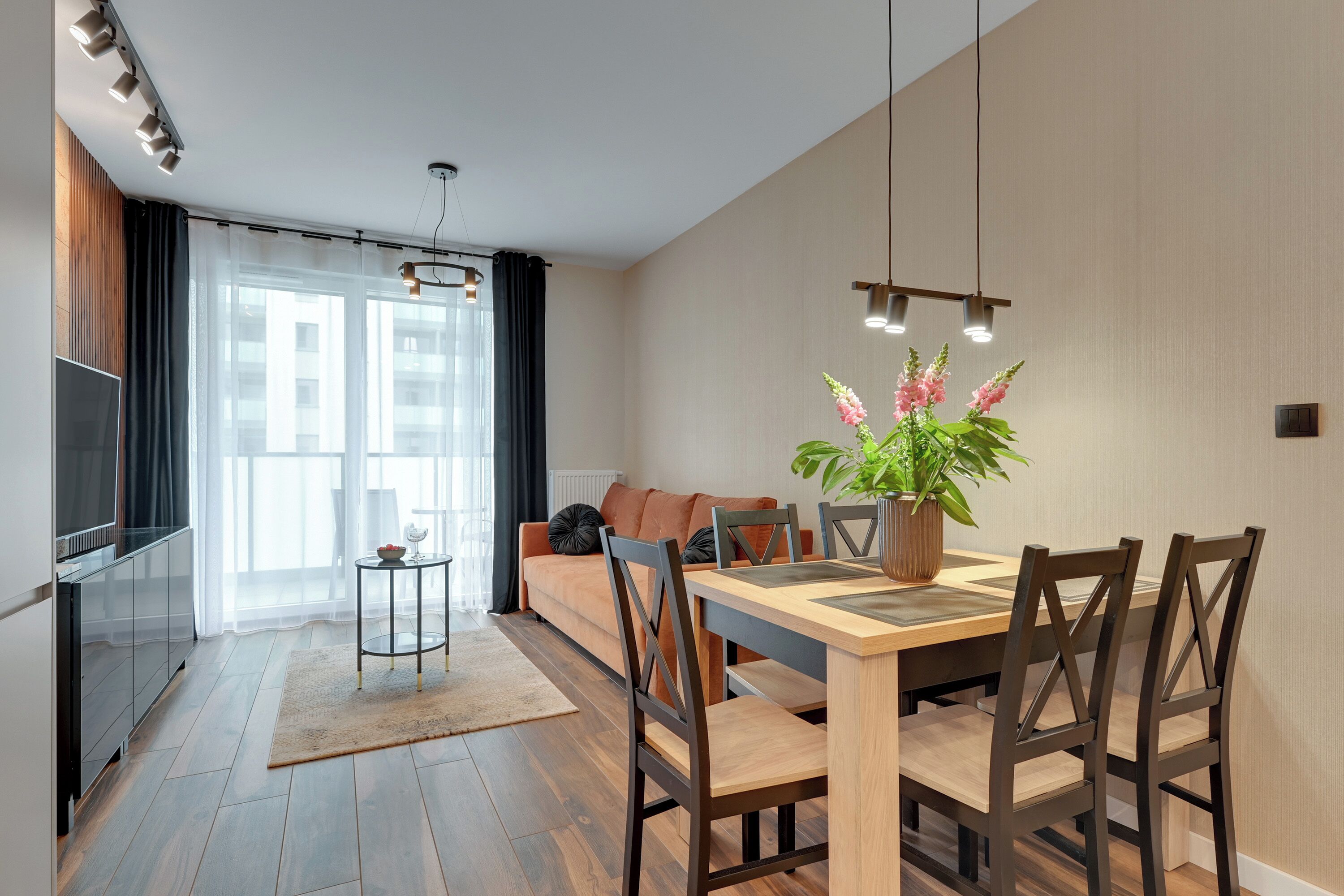 A modern living room with a sofa, dining table, chairs, a TV, and a potted plant.