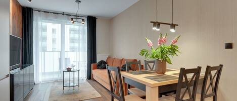 A modern living room with a sofa, dining table, chairs, a TV, and a potted plant.