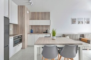 A modern kitchen with white cabinets, a wooden accent wall, and a dining area with a wooden table and two chairs.