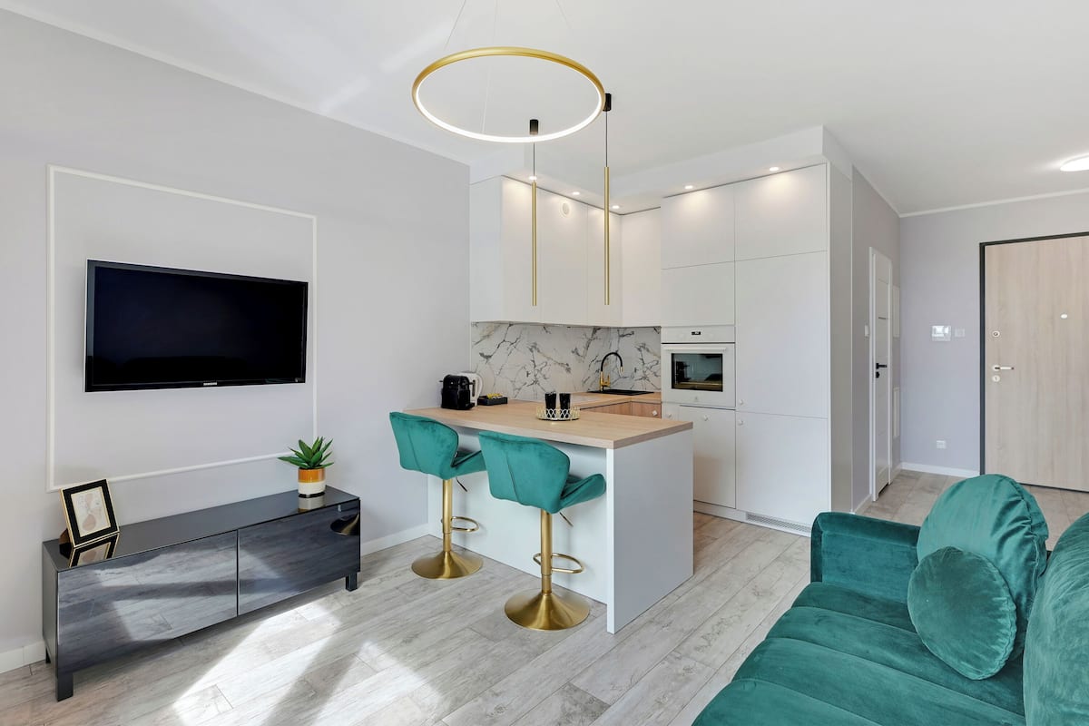 A modern kitchen with a marble backsplash, a central island with bar stools, and a flat-screen TV mounted on the wall.