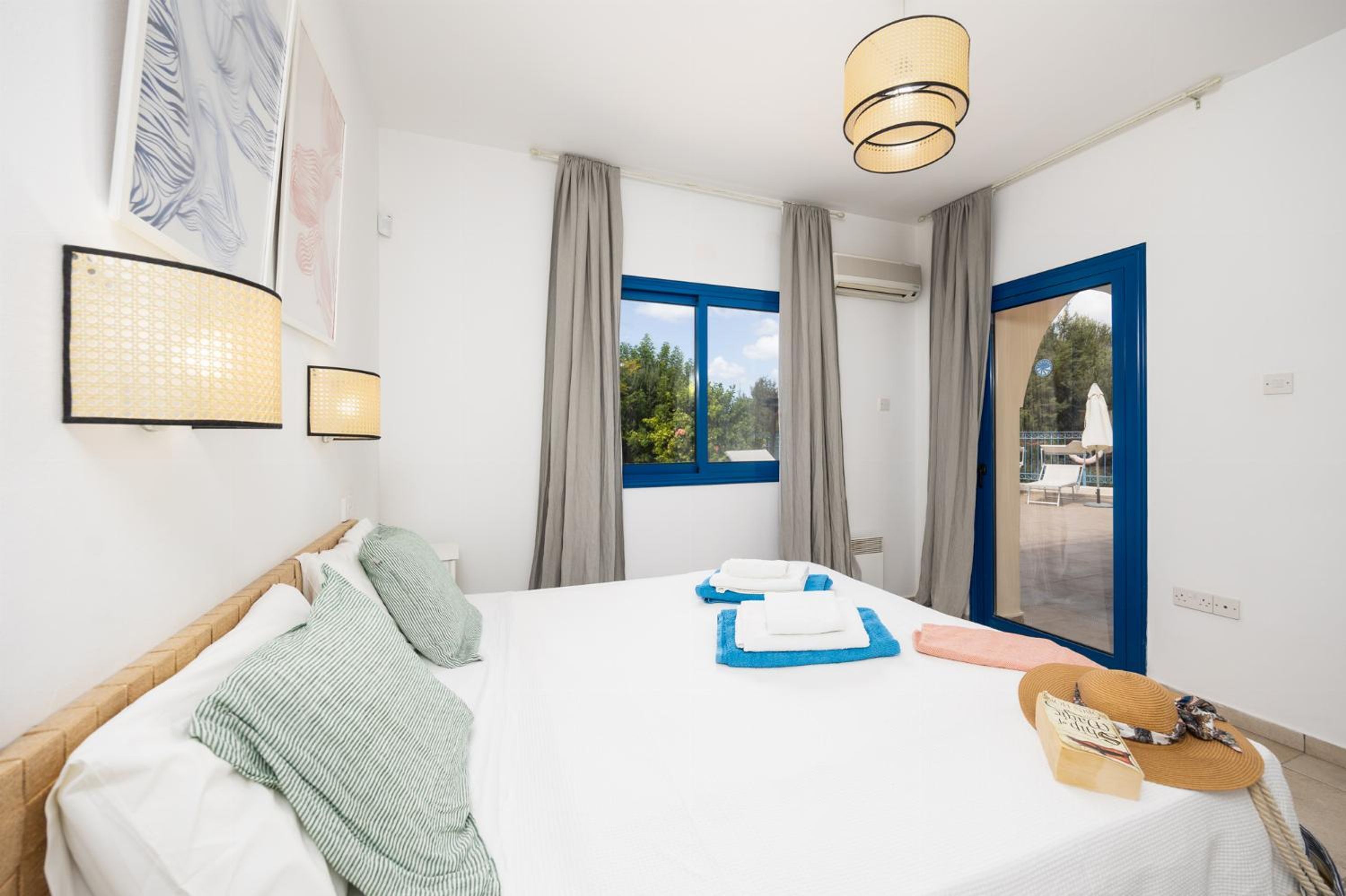 Habitación de hotel con cama, ventana con cortinas, lámpara de pared y vista al exterior.