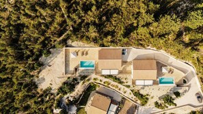 An aerial view of a resort with multiple buildings, including a main structure with a swimming pool and a separate building with a smaller pool. - Villa Hill View Ena in Paxi (Paxos)