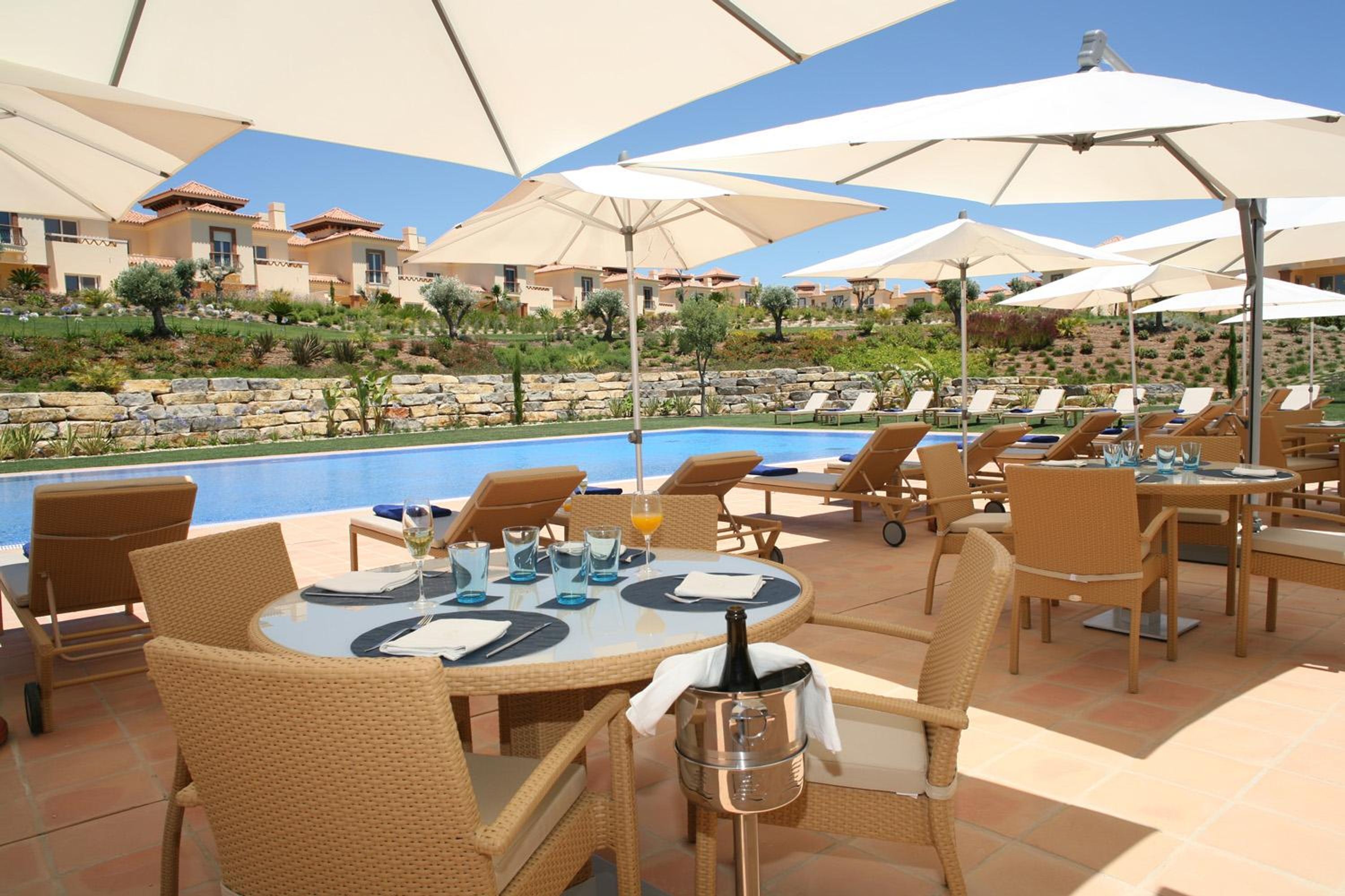 Ein Poolbereich mit Liegestühlen und Sonnenschirmen, ein Schwimmbecken und im Hintergrund eine Gebäudebeschichtung.