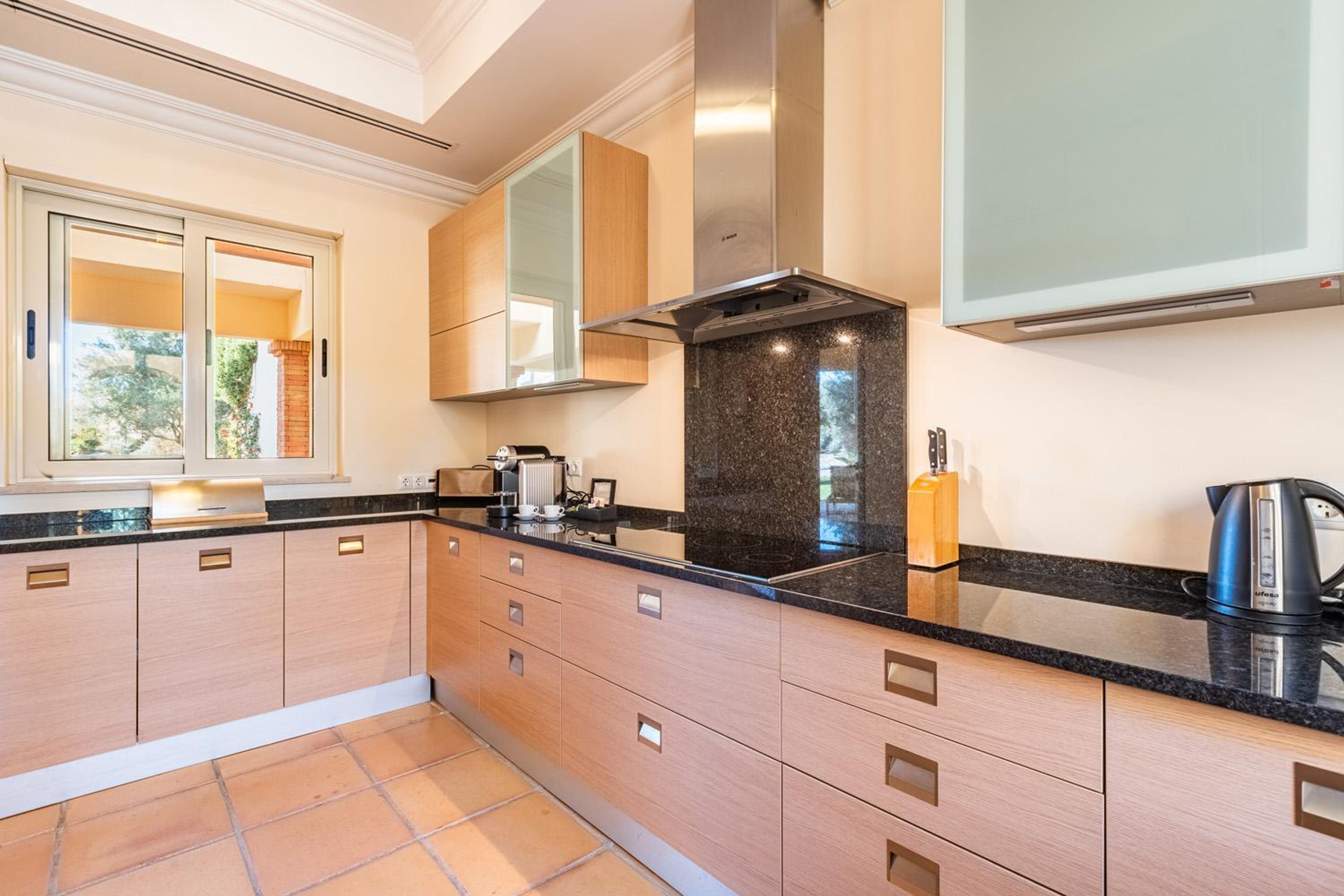A modern kitchen with wooden cabinets, a black countertop, and a stainless steel range hood.
