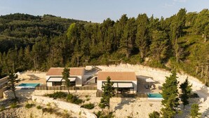 Un bâtiment à deux étages doté d’une piscine, entouré d’une zone sablonneuse et d’une forêt dense.