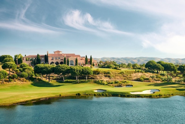 Una casa grande y lujosa con un campo de golf y un estanque al frente.
