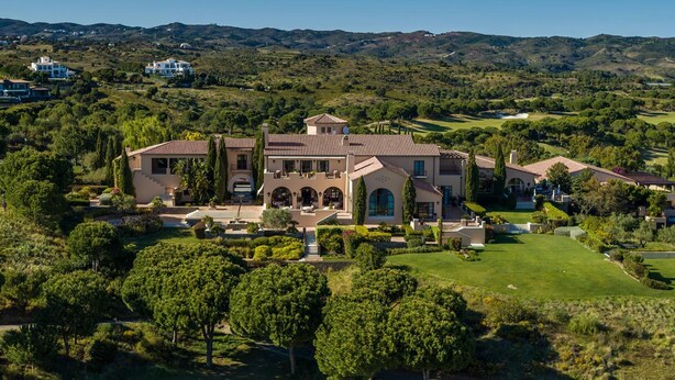 A large, multi-story house with a central courtyard, surrounded by lush greenery and hills in the background. - Villa Monte Rei 9 in Vila Nova de Cacela (Vila Real Santo Antonio)