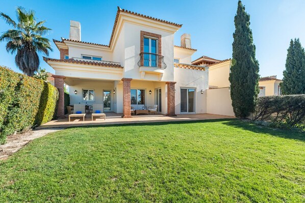 A two-story house with a balcony, a covered patio, and a well-maintained lawn.