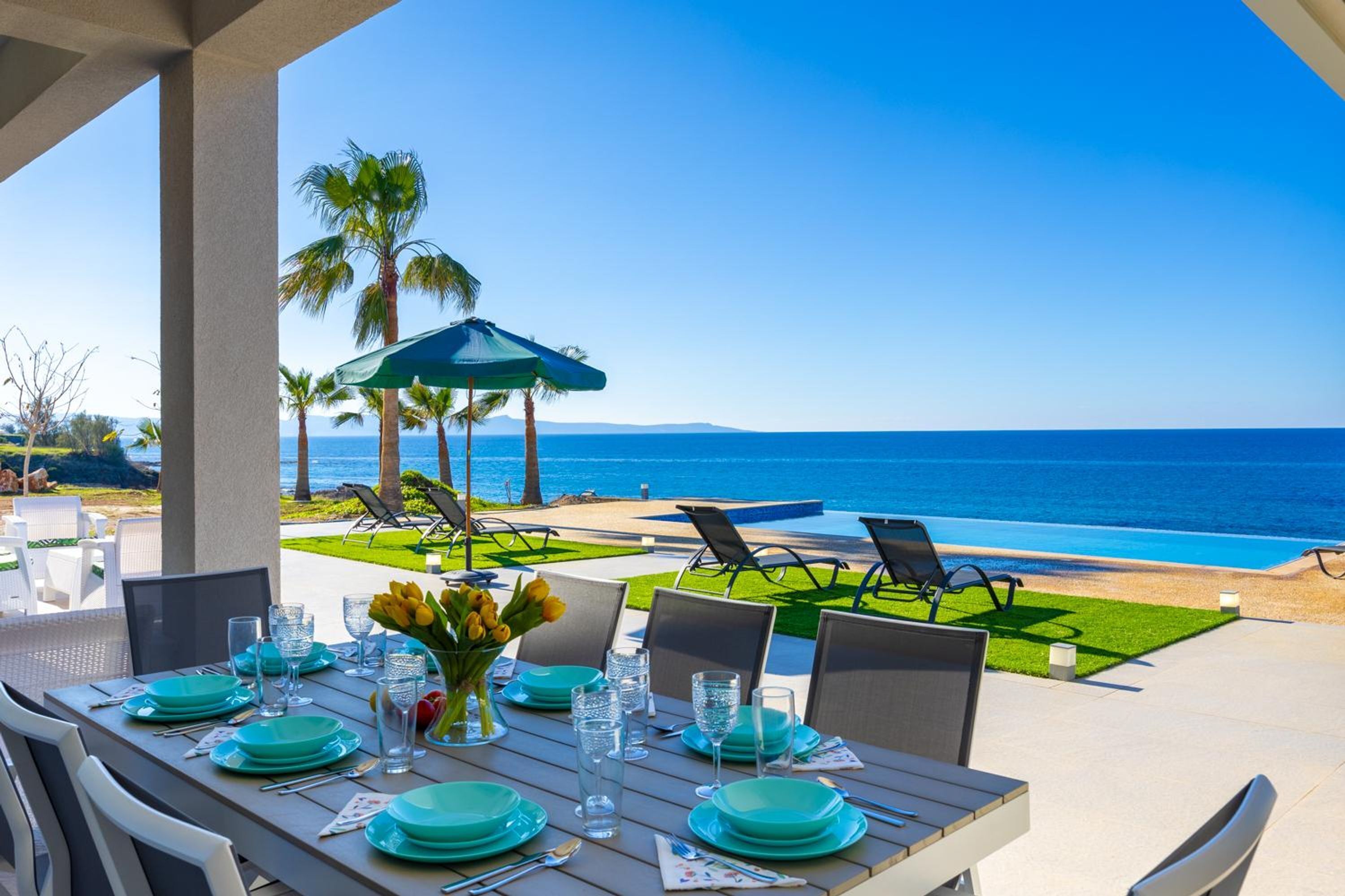 An outdoor dining area with a view of the ocean, equipped with tables, chairs, and umbrellas.