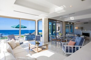 En moderne stue med en stor glasdør, der fører ud til en balkon med udsigt over havet.