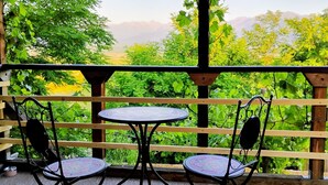 Een overdekt terras met twee ronde tafels en vier stoelen, met uitzicht op een weelderig landschap met bomen en verre bergen.